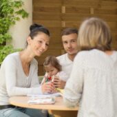 Familienpatin sitzt mit Eltern und Kind an einem Tisch